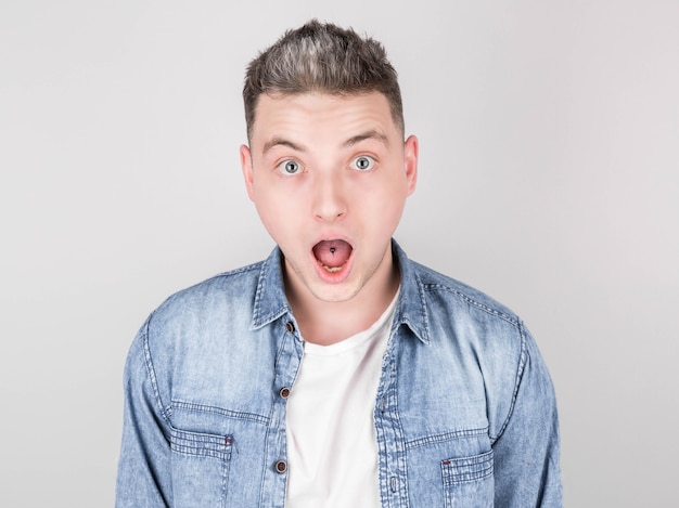 Porträt eines überraschten Mannes mit durchbohrter Zunge im Jeanshemd