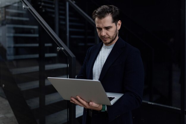 Porträt eines überzeugten europäischen Geschäftsmannes, der einen Laptop in seinen Händen gegen den Hintergrund von hält