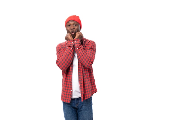 Porträt eines verwirrten schwarzen Amerikaners in rotem Hemd und Mütze, der vor weißem Hintergrund zuckt