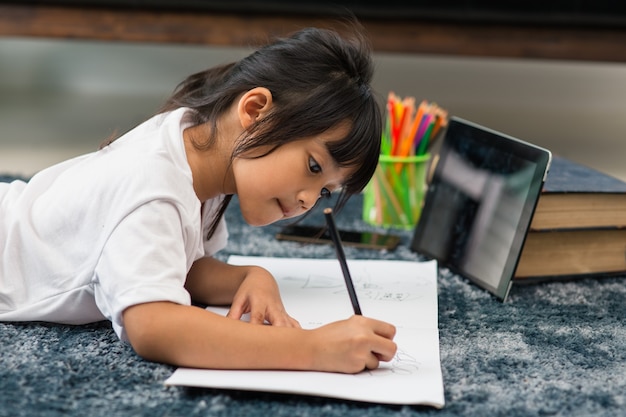 Porträt eines Vorschulkindes, das Tablet für seine Hausaufgaben verwendet, Weicher Fokus des Kindes, das Hausaufgaben macht, indem es digitale Tablets verwendet, um Informationen über das Internet, E-Learning oder das Bildungskonzept zu Hause zu suchen