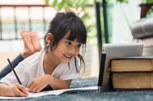 Porträt eines Vorschulkindes, das Tablet für seine Hausaufgaben verwendet, Weicher Fokus des Kindes, das Hausaufgaben macht, indem es digitale Tablets verwendet, um Informationen über das Internet, E-Learning oder das Bildungskonzept zu Hause zu suchen