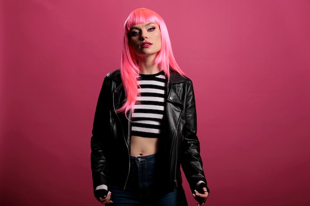 Porträt eines weiblichen Models mit stylischer Lederjacke im Studio, das sich im Punk-Rocker-Stil sorglos und sinnlich fühlt. Rosa Haare zu haben und funky zu sein, glamouröse, erstaunliche Mode über dem Hintergrund.