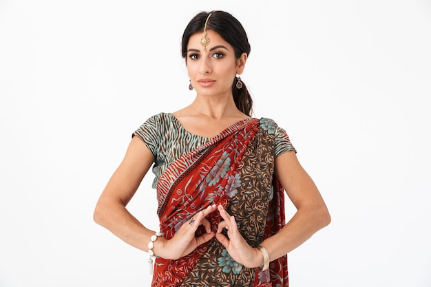 Porträt eines wunderschönen Hindu-Mädchens, das traditionelles indisches Saree-Kleid und ethnischen Schmuck trägt, der mit gestikulierenden Händen über weißer Wand tanzt?