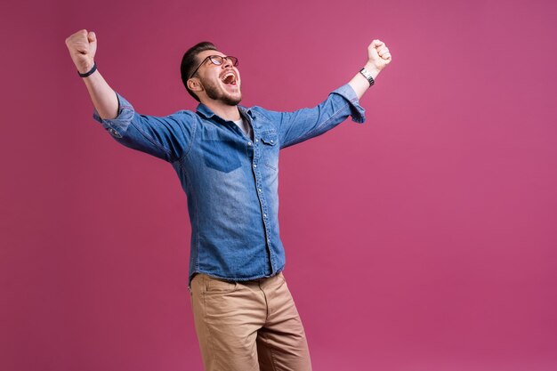 Porträt eines zufriedenen jungen Mannes, der Erfolg feiert, lokalisiert über rosa Hintergrund.