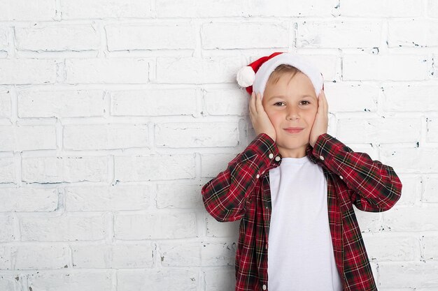 Porträt eines zufriedenen kleinen Jungen in Weihnachten Santa Hut lachend isoliert über gelbem Hintergrund Hält eine Geschenkbox Vorbereitung für die Neujahrsferien