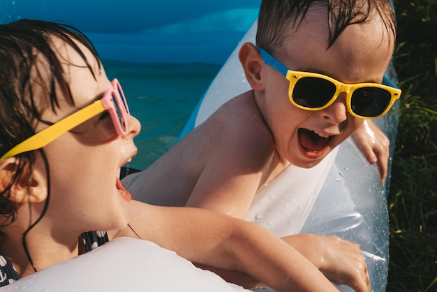 Porträt fröhlicher lachender Kinder in Sonnenbrillen im Schwimmbad an einem heißen Sommertag