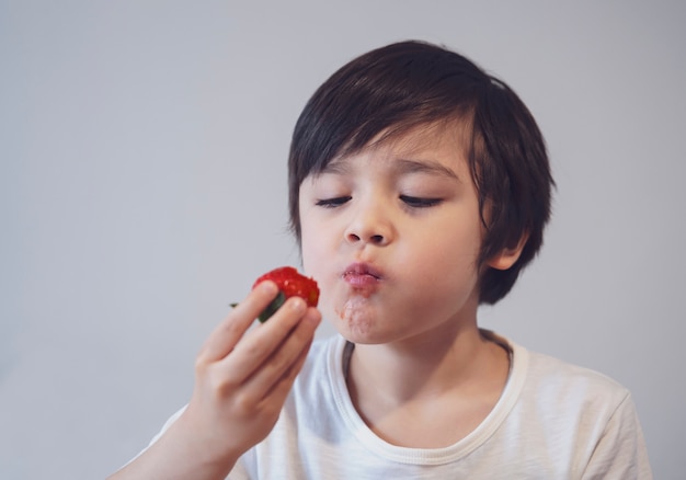 Porträt Gesundes Kind, das Erdbeeren isst, selektiver Fokus Hungriger kleiner Junge, der Erdbeere auf seiner Hand mit lächelndem Gesicht betrachtet, Kind, das frische Erdbeere schmeckt, gesundes Sommeressen für Kinder