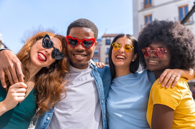 Porträt glücklicher multiethnischer Freunde mit Herzsonnenbrillen auf der Straße der Stadt, die draußen zusammen lachen