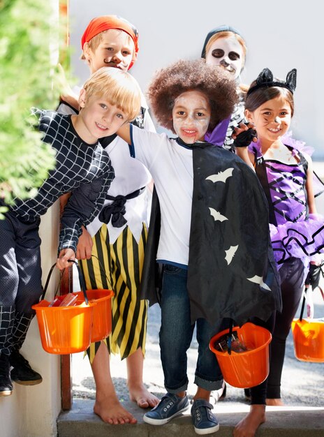 Foto porträt halloween und gruppe von kindern in kostümen für trick or treat tradition in der nachbarschaft zusammen lächeln süßigkeiten und freunde mit kleinen kindern in schicken kleidern für urlaub oder urlaub feiern