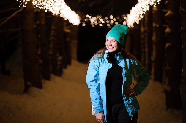 Porträt im Freien des glücklichen lächelnden Mädchens. Vorbildliche Aufstellung im Nachtpark mit Weihnachtslichtern. Winterurlaub-Konzept.