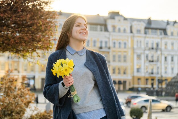Porträt im Freien des jungen schönen Mädchens mit Blumenstrauß von gelben Frühlingsblumen