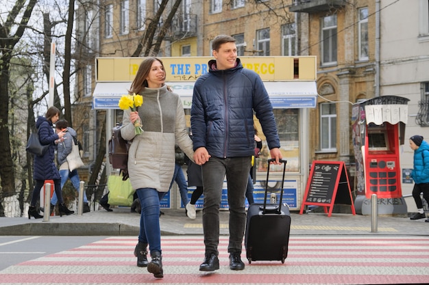 Porträt im freien von den jungen paaren, die mit koffer auf stadt gehen