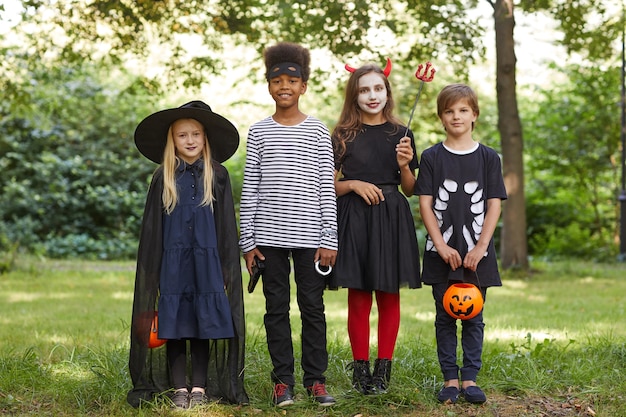 Porträt in voller Länge einer multiethnischen Gruppe von Kindern, die Halloween-Kostüme tragen, während sie im Freien stehen und