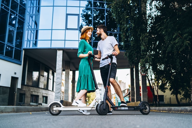 Porträt in voller Länge eines jungen romantischen Paares mit Elektrorollern an einem Datum, das in der Stadt geht.