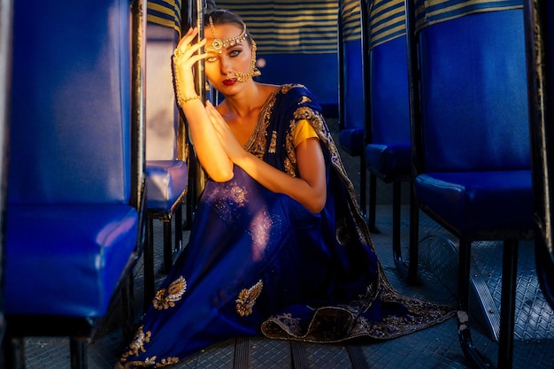Porträt indische schöne kaukasische Frau im traditionellen blauen Kleid. Hindu-Modell mit goldenem Kundan-Schmuckset Bindi-Ohrringen und Nasenring-Piercing nath Mode-Fotoshooting im Bus