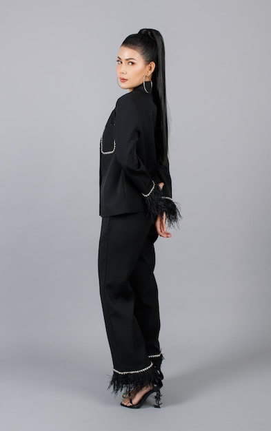 Porträt isolierte Ausschnitt-Studioaufnahme eines tausendjährigen asiatischen weiblichen eleganten Modemodells in schwarzem, lässigem, modischem Pelzanzug, der posiert und Blick in die Kamera auf grauem Hintergrund posiert