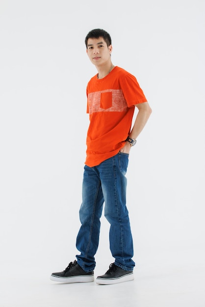 Porträt, isoliertes Ausschnitt, Studio-Shooting, asiatisches schlaues, hübsches männliches Modemodell in Casual-Outfit, T-Shirt und Blue-Jeans, posierend, Hand in der Tasche, lächelnd, auf weißen Hintergrund in die Kamera schauend