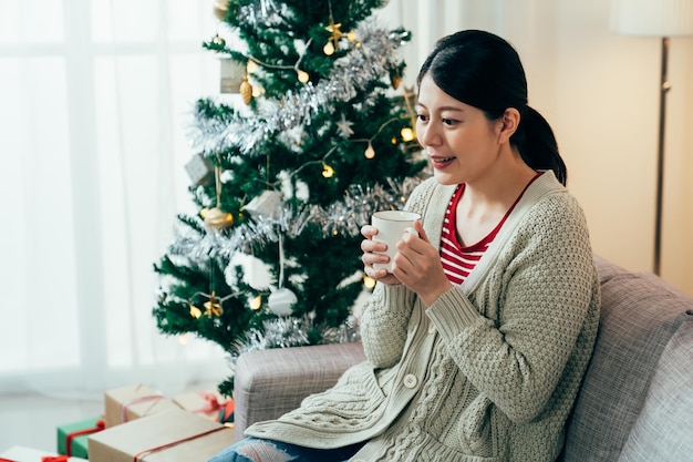 porträt japanische tausendjährige frau, die becher mit beiden händen zu hause hält. asiatische dame, die sich an einem kalten tag mit heißer schokolade aufwärmt. echte Momente