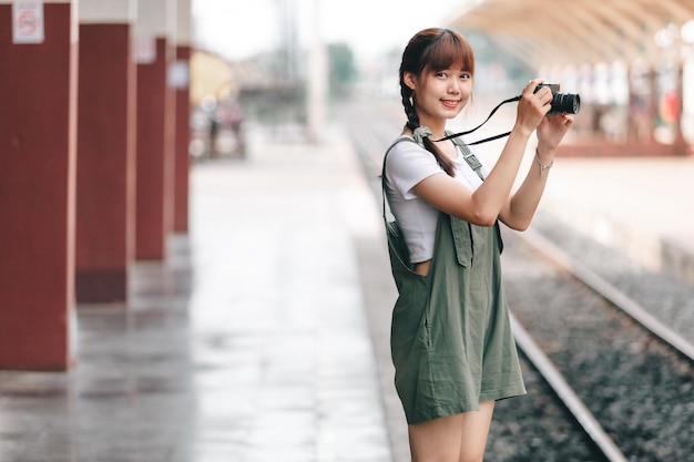 Porträt Junge asiatische Frau, die Tourist lächelt Reisendes Mädchen, das zu Fuß geht und mit einer Kamera wartet, die mit dem Zug unterwegs ist, wird im Bahnsteig Thailand-Sommerurlaubskonzept aufgenommen