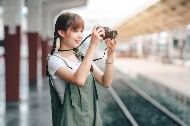 Porträt Junge asiatische Frau, die Tourist lächelt Reisendes Mädchen, das zu Fuß geht und mit einer Kamera wartet, die mit dem Zug unterwegs ist, wird im Bahnsteig Thailand-Sommerurlaubskonzept aufgenommen