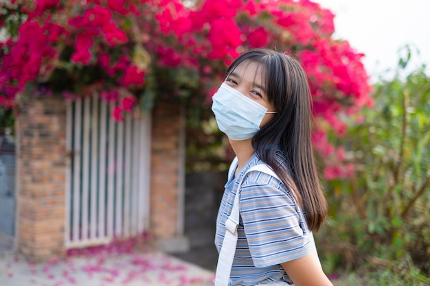 Porträt Junge asiatische Mädchen tragen Maske im Freien schönen Blumenhintergrund