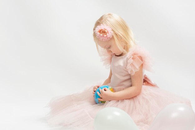 Porträt kleines blondes Mädchen sieht begeistert Globus in Händen Kind in rosa Kleid isoliert auf weißem Hintergrund
