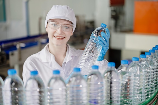 Porträt lächelnder junger kaukasischer Arbeiterin mit Getränkeflaschen arbeitet an der Fabrikproduktionslinie dri