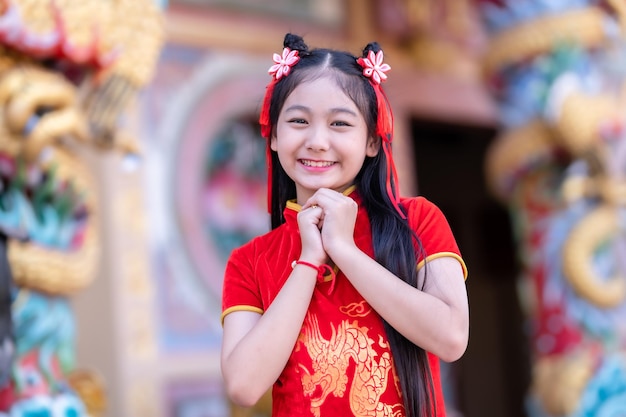 Porträt lächelt Niedliches kleines asiatisches Mädchen, das rotes Cheongsam-Kleid trägt, traditionelle Dekoration für das chinesische Neujahrsfest, feiert die Kultur Chinas im chinesischen Schrein