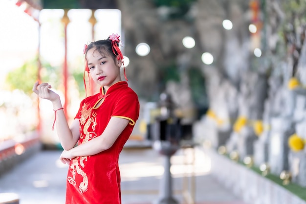Porträt lächelt Niedliches kleines asiatisches Mädchen, das rotes Cheongsam-Kleid trägt, traditionelle Dekoration für das chinesische Neujahrsfest, feiert die Kultur Chinas im chinesischen Schrein