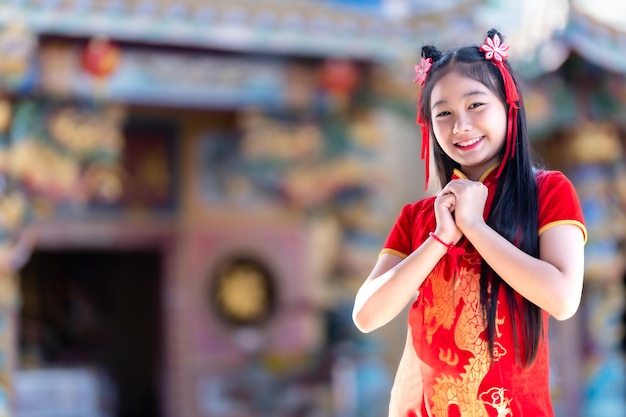 Porträt lächelt Niedliches kleines asiatisches Mädchen, das rotes Cheongsam-Kleid trägt, traditionelle Dekoration für das chinesische Neujahrsfest, feiert die Kultur Chinas im chinesischen Schrein