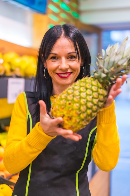 Porträt mit Ananas in der Hand eines brünetten kaukasischen Obstmädchens, das in einem Obstladen arbeitet