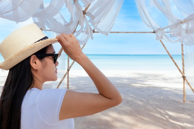 Porträt-Mittelschussansicht der Frau stehen im weißen T-Shirt und im Hut, die in Richtung blauen Ozean und Himmel schauen