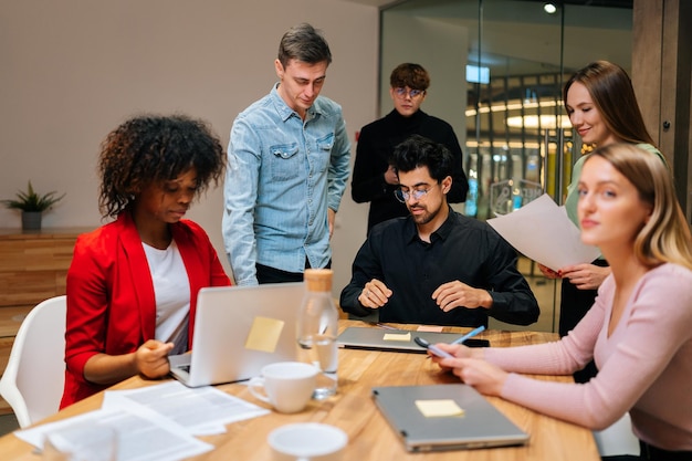 Porträt multiethnischer männlicher und weiblicher Kollegen, die bei einer Sitzung im Sitzungssaal mit Projektdokumenten arbeiten und am Tisch sitzen und Statistiken analysieren