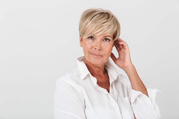 Porträt-Nahaufnahme einer eleganten erwachsenen Frau mit kurzen blonden Haaren, die isoliert über die weiße Wand im Studio in die Kamera schaut