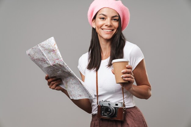 Porträt-Nahaufnahme einer freundlichen jungen Touristenfrau mit Retro-Vintage-Kamera und Kaffee zum Mitnehmen lächelt und hält Papierkarte isoliert über grauer Wand
