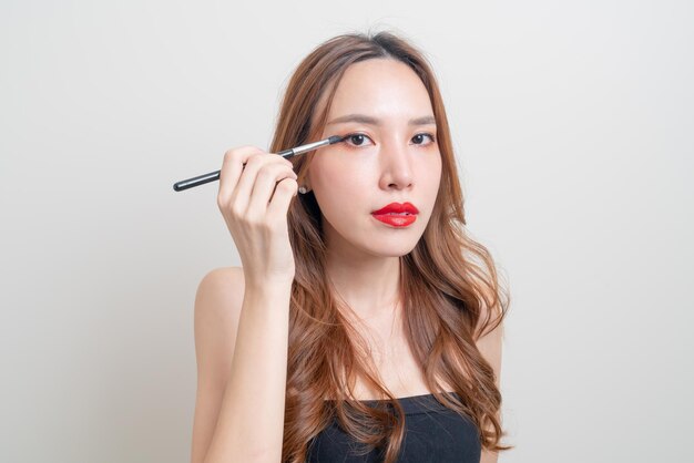 Porträt schöne asiatische frau mit make-up-augenbürste auf weißem hintergrund