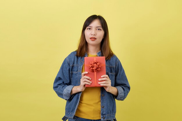 Porträt schöne junge asiatische Frau mit roter Geschenkbox auf gelb isoliert