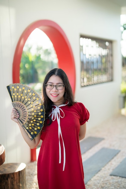 Porträt schöne lächelnde asiatische junge Frau trägt rote traditionelle chinesische Dekoration und hält einen chinesischen Fanning für das chinesische Neujahrsfest im chinesischen Restaurantcafé