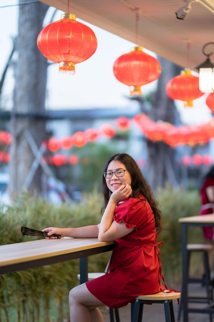 Porträt schöne lächelnde asiatische junge Frau trägt rote traditionelle chinesische Dekoration und hält einen chinesischen Fanning für das chinesische Neujahrsfest im chinesischen Restaurantcafé