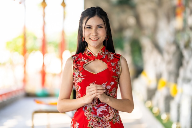 Porträt schöne lächelt asiatische junge Frau, die rotes traditionelles chinesisches cheongsam trägt, für chinesisches Neujahrsfest am chinesischen Schrein