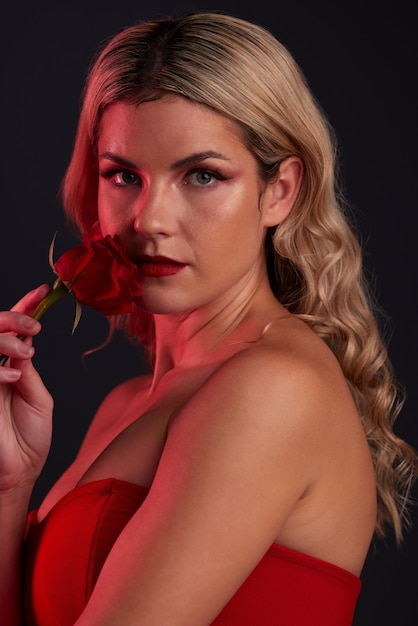 Porträt Schönheit und Rose mit einer Modelfrau im Studio auf einem dunklen Hintergrund für den Valentinstag Gesichtshautpflege oder Blume mit einer jungen weiblichen Person, die in Rot posiert für natürliches weibliches Selbstvertrauen