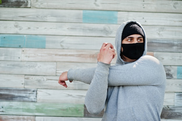 Porträt sportlicher arabischer Mann in der schwarzen medizinischen Gesichtsmaske und im Kapuzenpulli während der Coronavirus-Quarantäne.