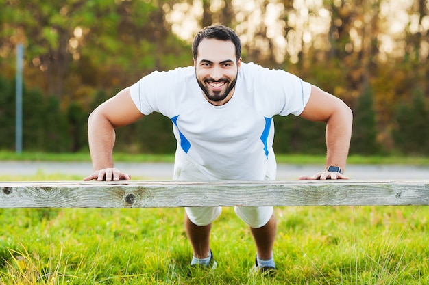 Porträt sportlicher Mann 30s in der Sportbekleidung, die Liegestütze im grünen Park tut.