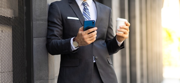 Porträt Stilvoller Hipster bärtiger Geschäftsmann im Anzug, der Kaffee trinkt und Smartphone benutzt. Menschen, die techniksüchtig sind