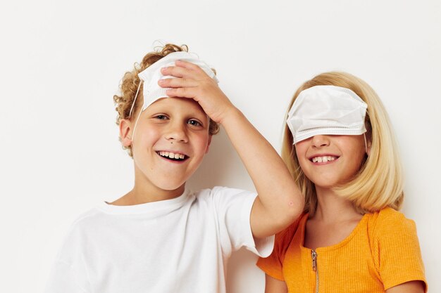 Porträt süßer Kinder im medizinischen Maskenschutz, die vor hellem Hintergrund Grimassen posieren