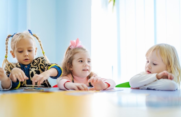 Porträt süßer kleiner Vorschulmädchen, die mit gefalteten Händen am Schreibtisch im Klassenzimmer sitzen und spielen und lernen Vorschulkonzept