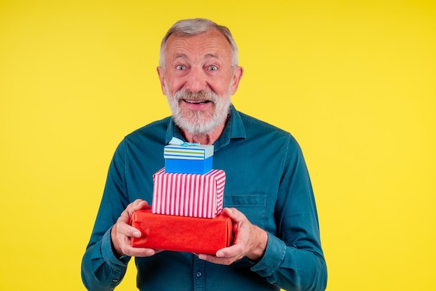 Porträt überraschte den kaukasischen alten älteren Mann, der zwei Boxex Geschenke im gelben Studiohintergrund hält.