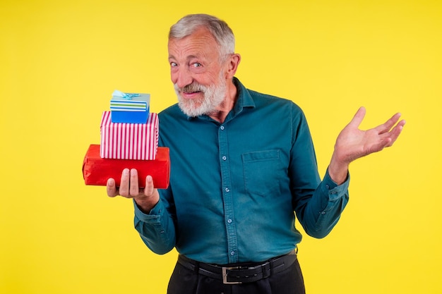 Foto porträt überraschte den kaukasischen alten älteren mann, der zwei boxex geschenke im gelben studiohintergrund hält.