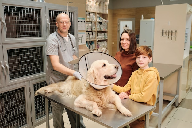 Porträt von Besitzern, die in der Tierklinik in die Kamera lächeln, während der Arzt ihren Hund untersucht