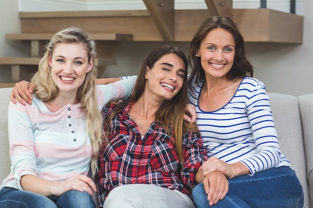 Porträt von den Freunden, die zusammen auf Sofa mit dem Arm herum sitzen